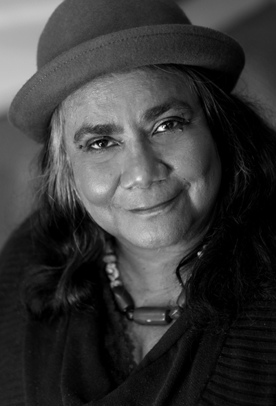 Black & white portrait of Gayle Kennedy smiling and wearing a hat and a necklace with large beads